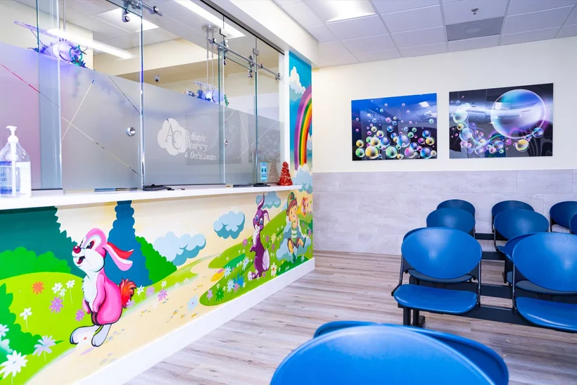 Pediatric Dentistry — Reception counter with a mural of rabbits and a rainbow, facing rows of blue waiting chairs
