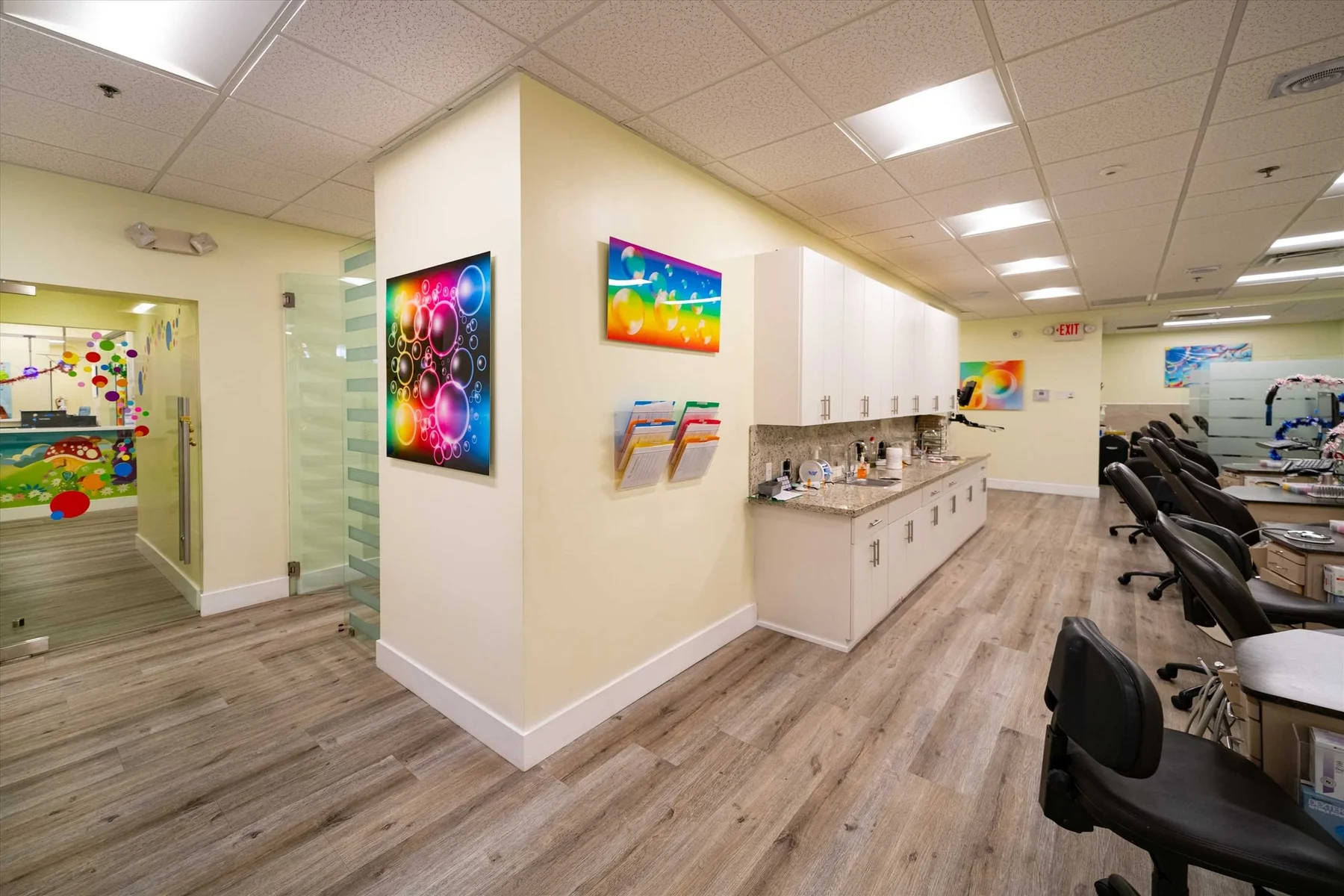 AC Pediatric Dentistry & Orthodontics — Open treatment area with a row of black dental chairs beside white cabinets and bubble art panels
