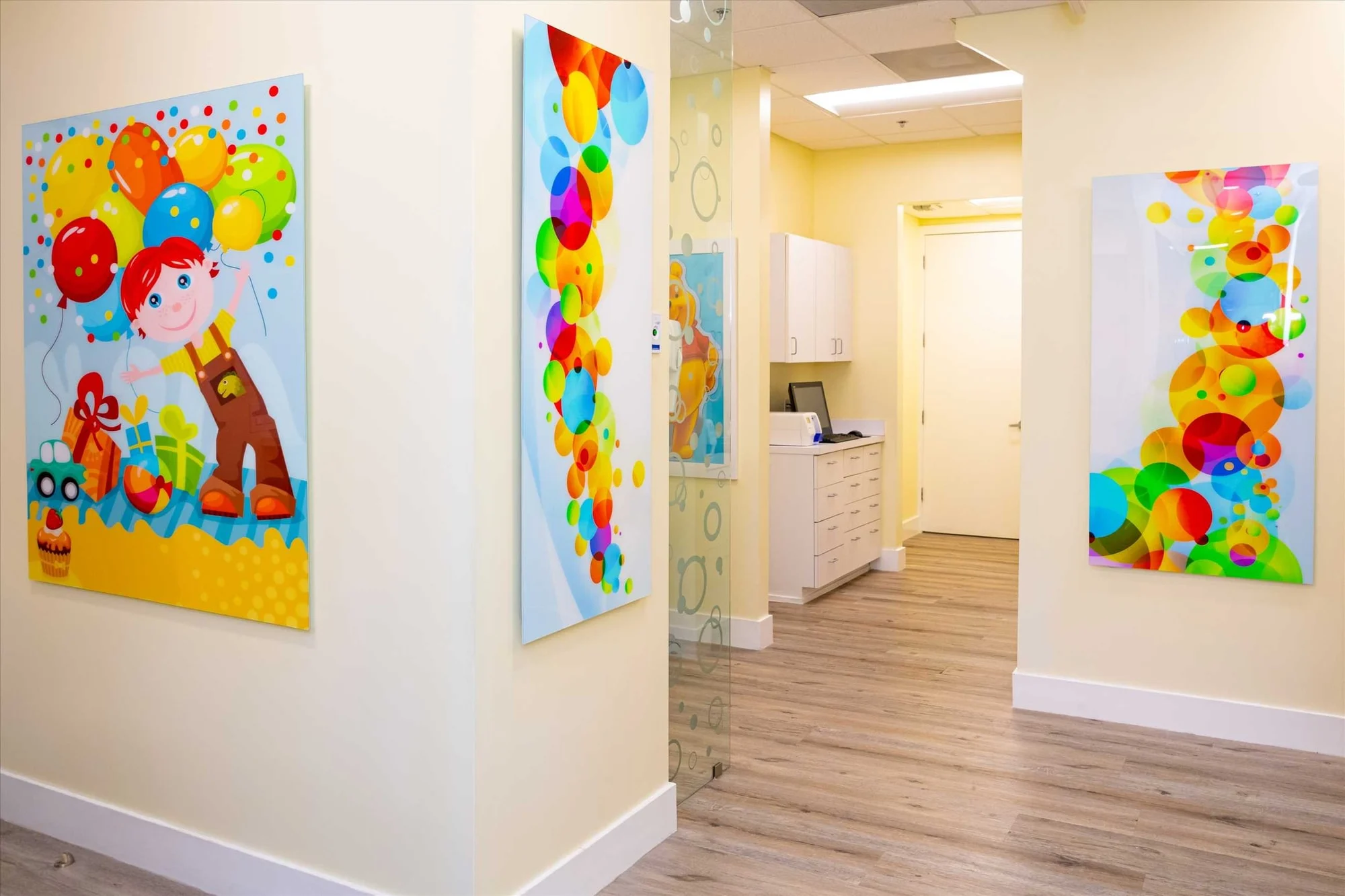 AC Pediatric Dentistry & Orthodontics — Hallway with a cartoon panel of a boy with balloons and tall multicolor bubble panels leading to a white workstation