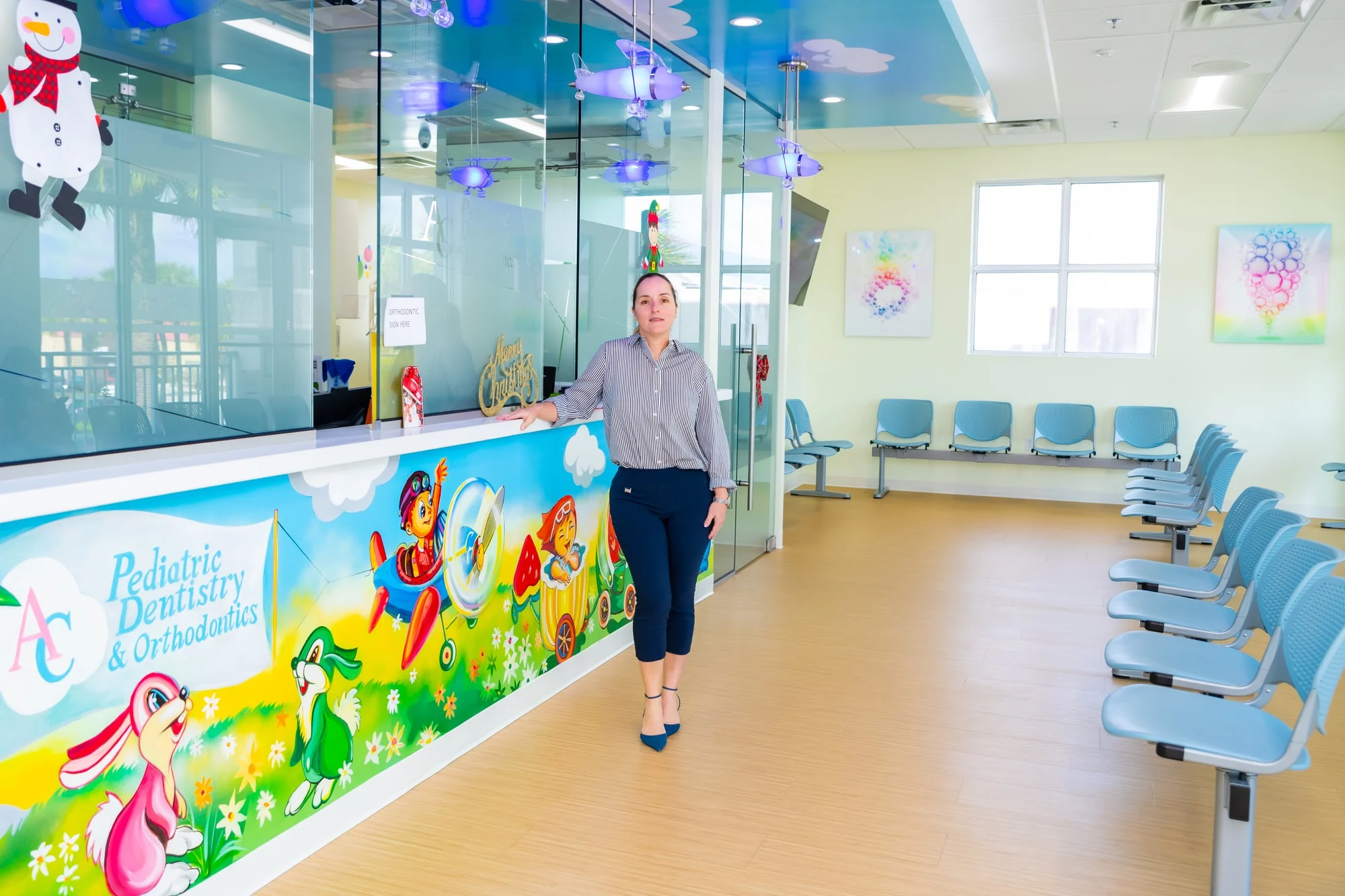 AC Pediatric Dentistry & Orthodontics — Reception counter with a cartoon mural and the “AC Pediatric Dentistry & Orthodontics” logo, with a person beside it
