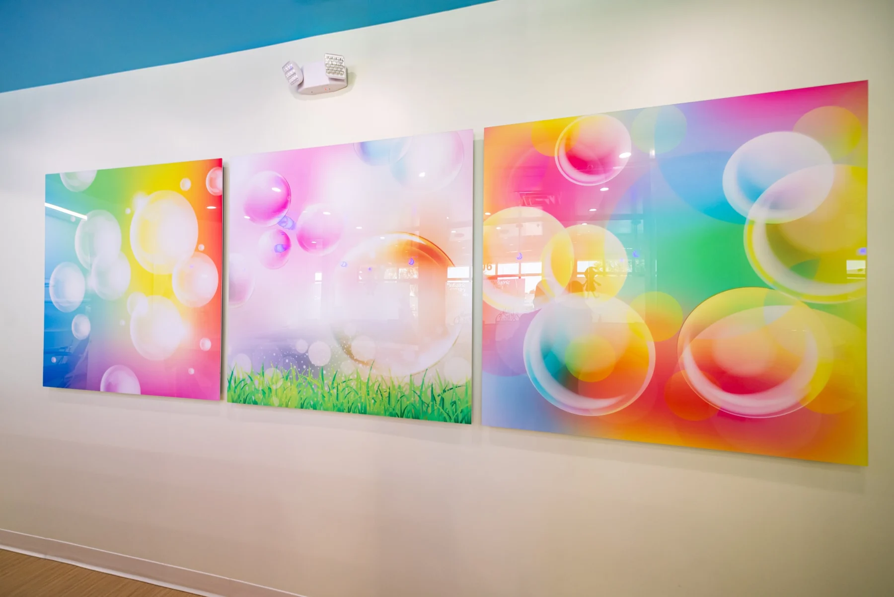 AC Pediatric Dentistry & Orthodontics — Detail of three glossy art panels with colorful bubbles on a white wall below the blue ceiling