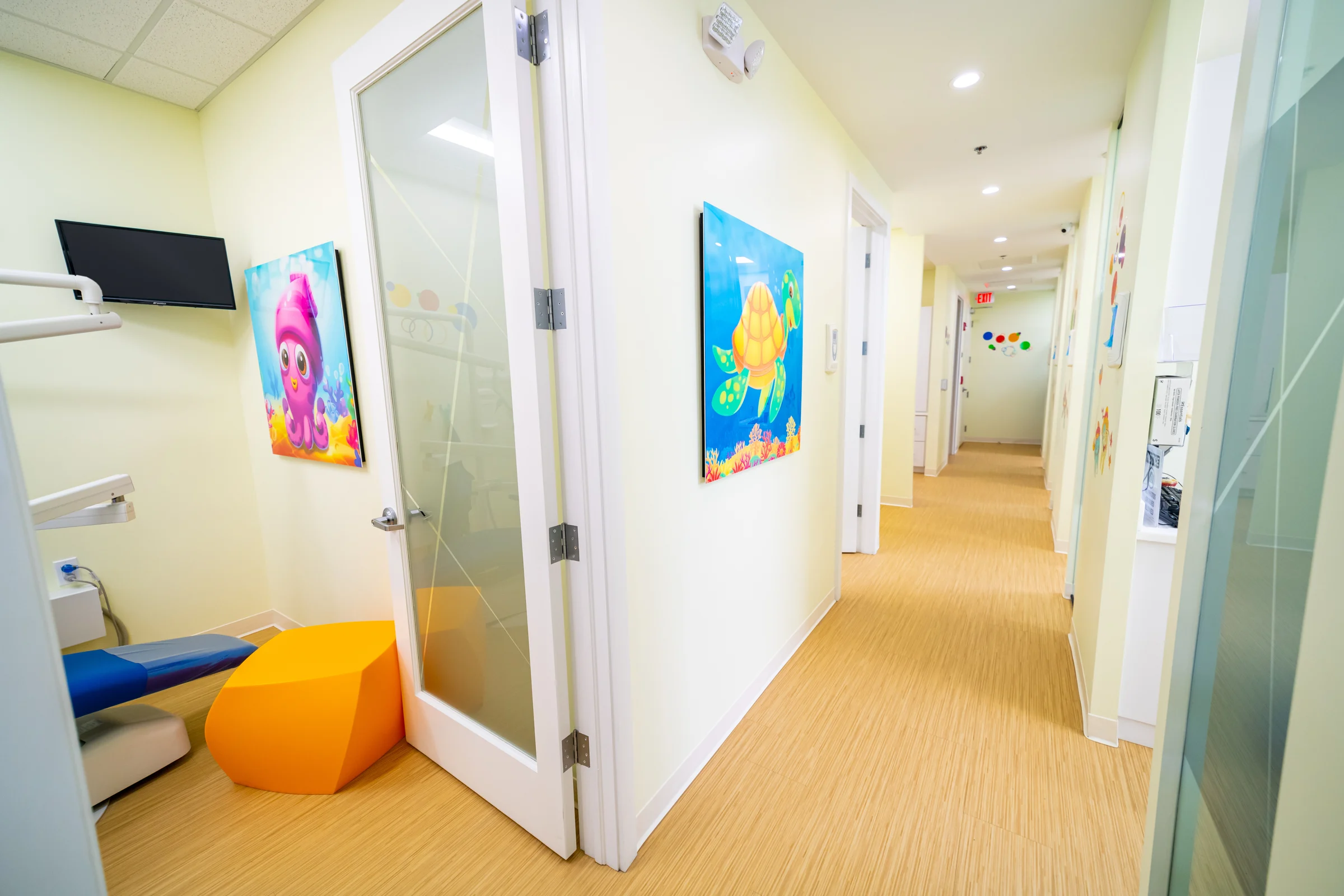 AC Pediatric Dentistry & Orthodontics — Corridor with sea-creature art panels and an open glass door to a treatment room with an orange stool