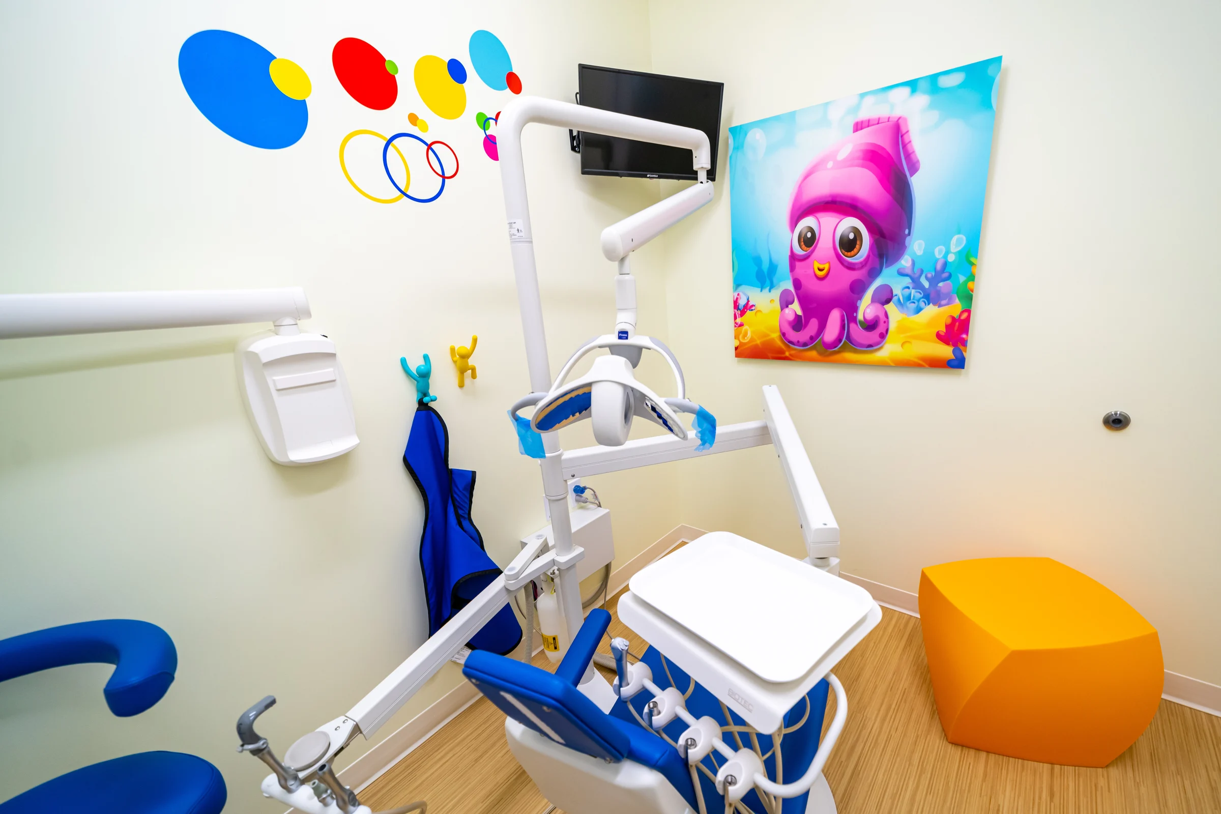 AC Pediatric Dentistry & Orthodontics — Close-up of a dental chair and light beside a pink squid art panel and colorful dot decals