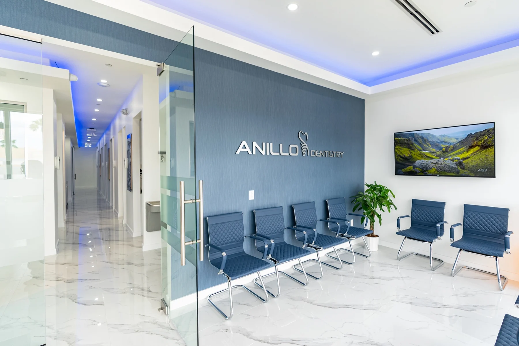 Anillo Dentistry — Mampara de vidrio y pasillo junto a la sala de espera, bajo una cornisa de luz azul