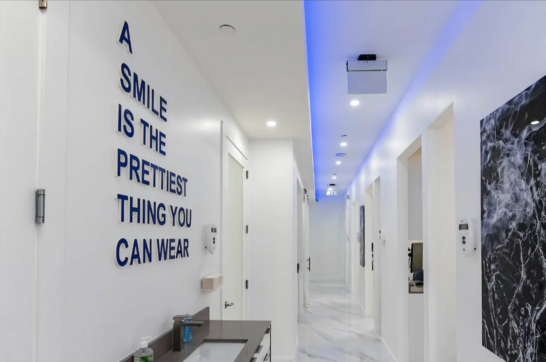 Anillo Dentistry — Pasillo con la frase A SMILE IS THE PRETTIEST THING YOU CAN WEAR en letras azul marino, junto a un lavamanos