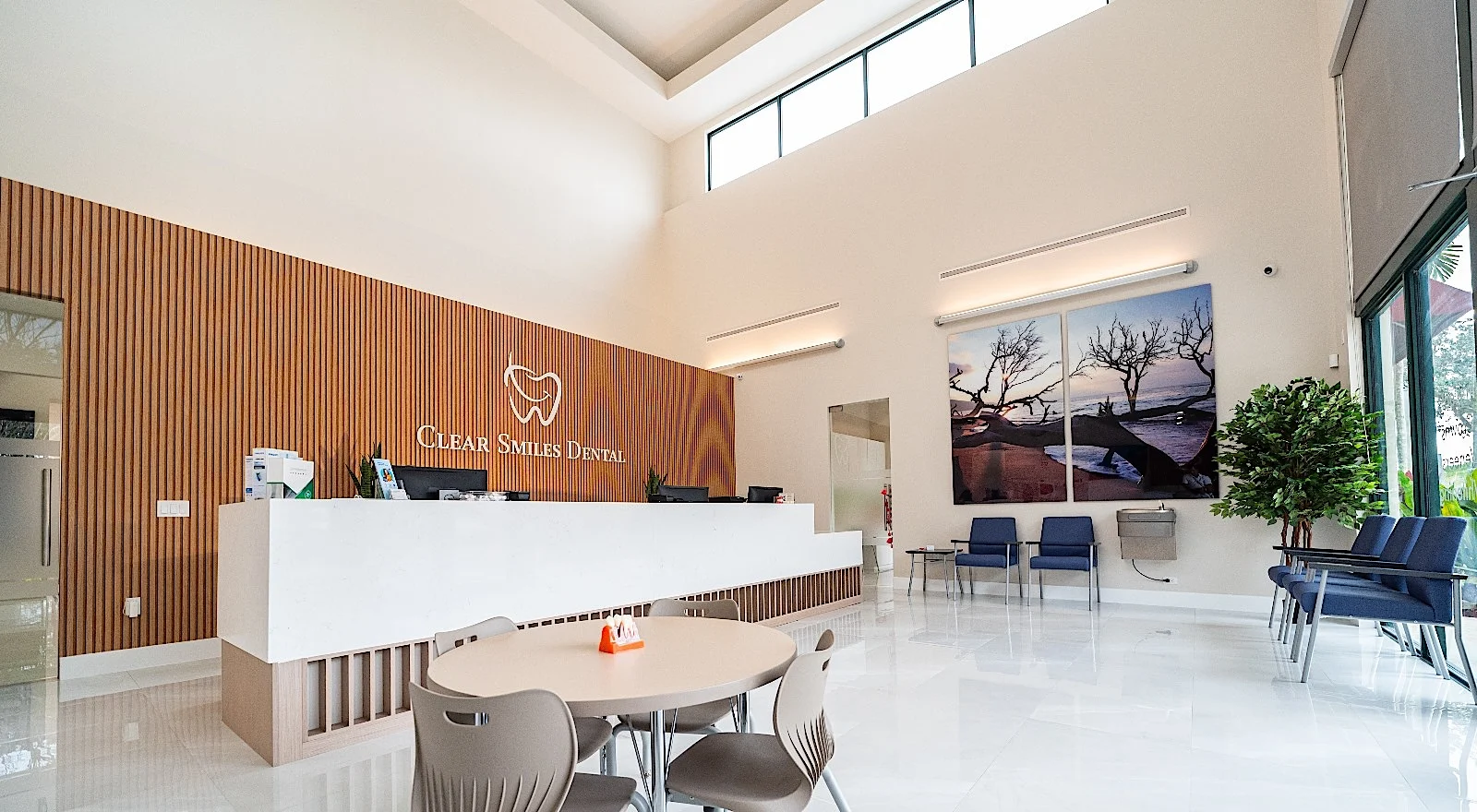 Clear Smiles Dental — Vista amplia de la recepción con una mesa redonda, la pared de listones y las ventanas altas