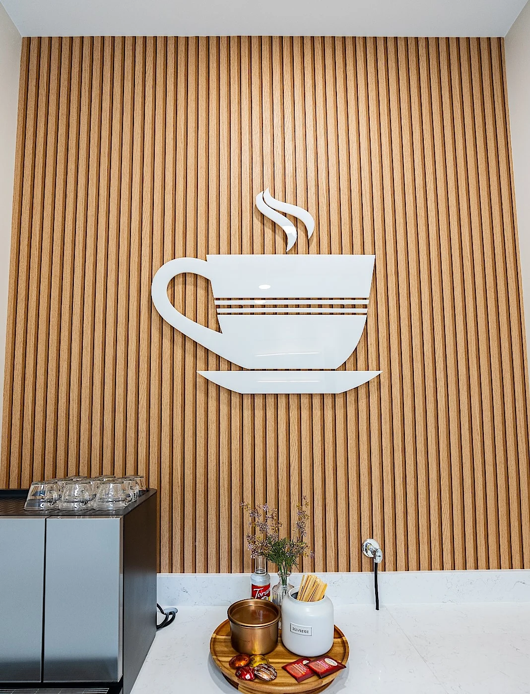 Clear Smiles Dental — Estación de café con una taza blanca en relieve sobre una pared de listones de roble