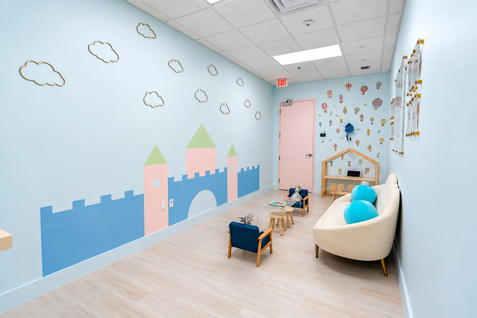 Denti Pediatric Dentistry — Waiting room with a painted castle mural, wooden cloud outlines and a cream sofa with turquoise cushions