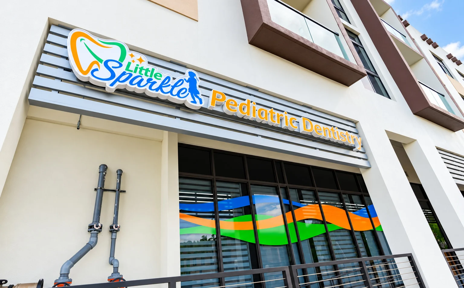 Little Sparkle Pediatric Dentistry — Facade with a dimensional sign over windows crossed by a band of blue, green and orange waves