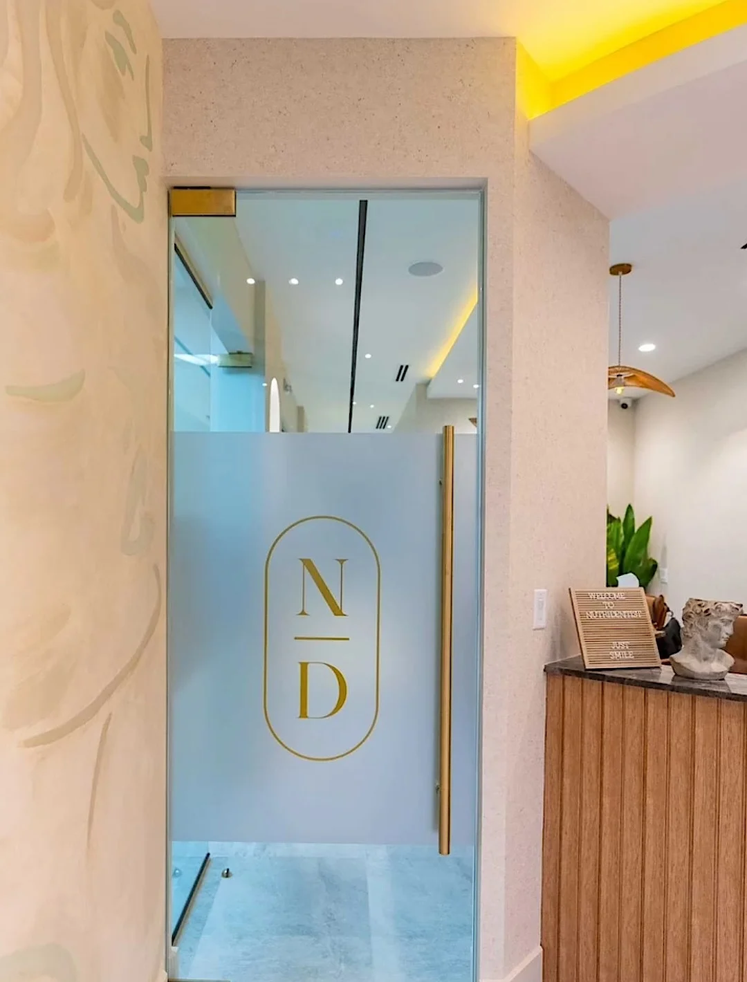 Nutridentist — Puerta de vidrio con una franja esmerilada y el monograma N/D dorado, junto al mostrador de recepción