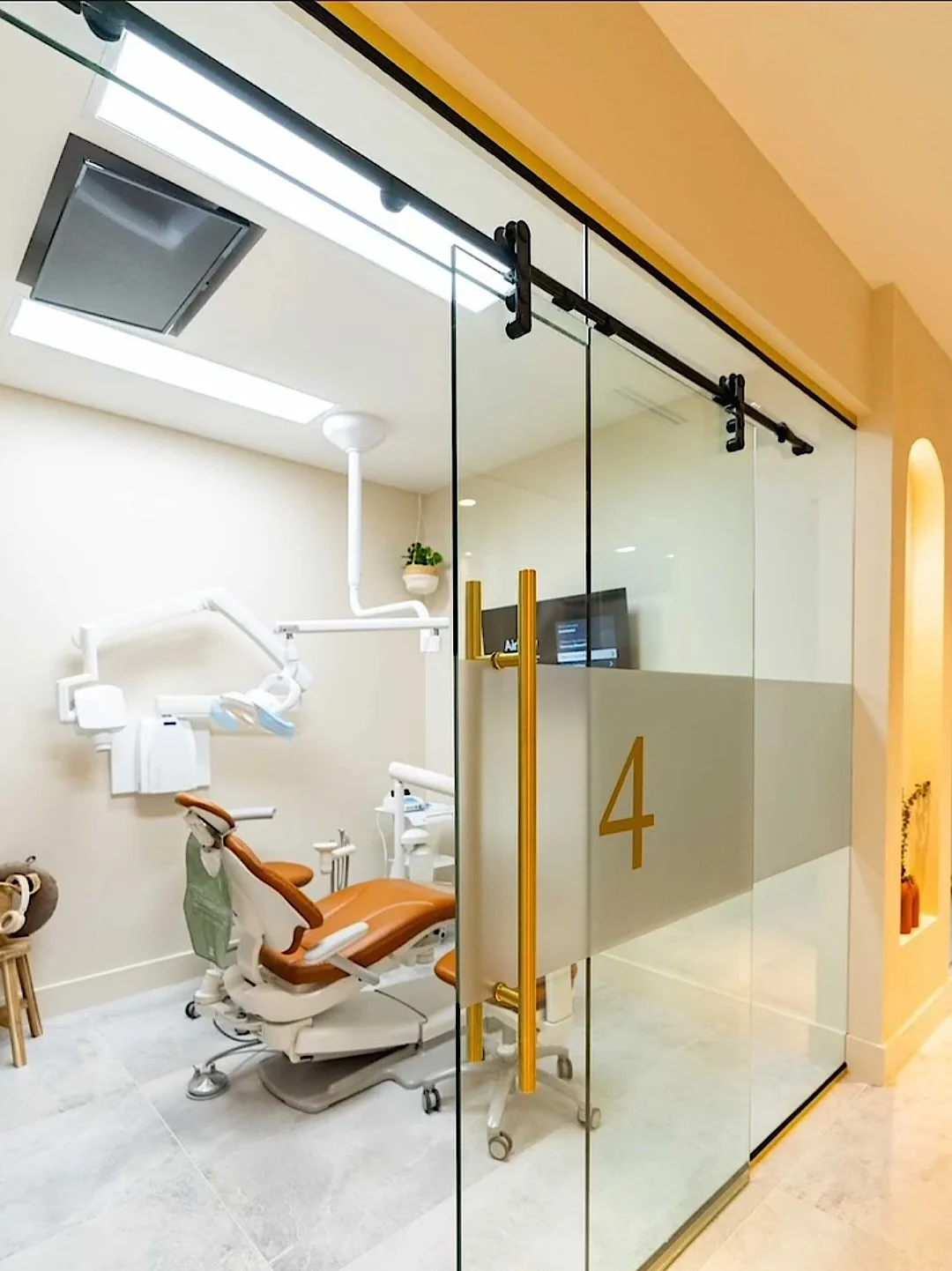 Nutridentist — Puerta corrediza de vidrio con el número 4 y tiradores dorados, delante de una sala de tratamiento con sillón color óxido