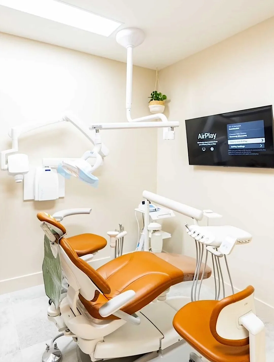 Nutridentist — Sala de tratamiento con sillón dental color óxido, lámpara colgada del techo y pantalla en la pared