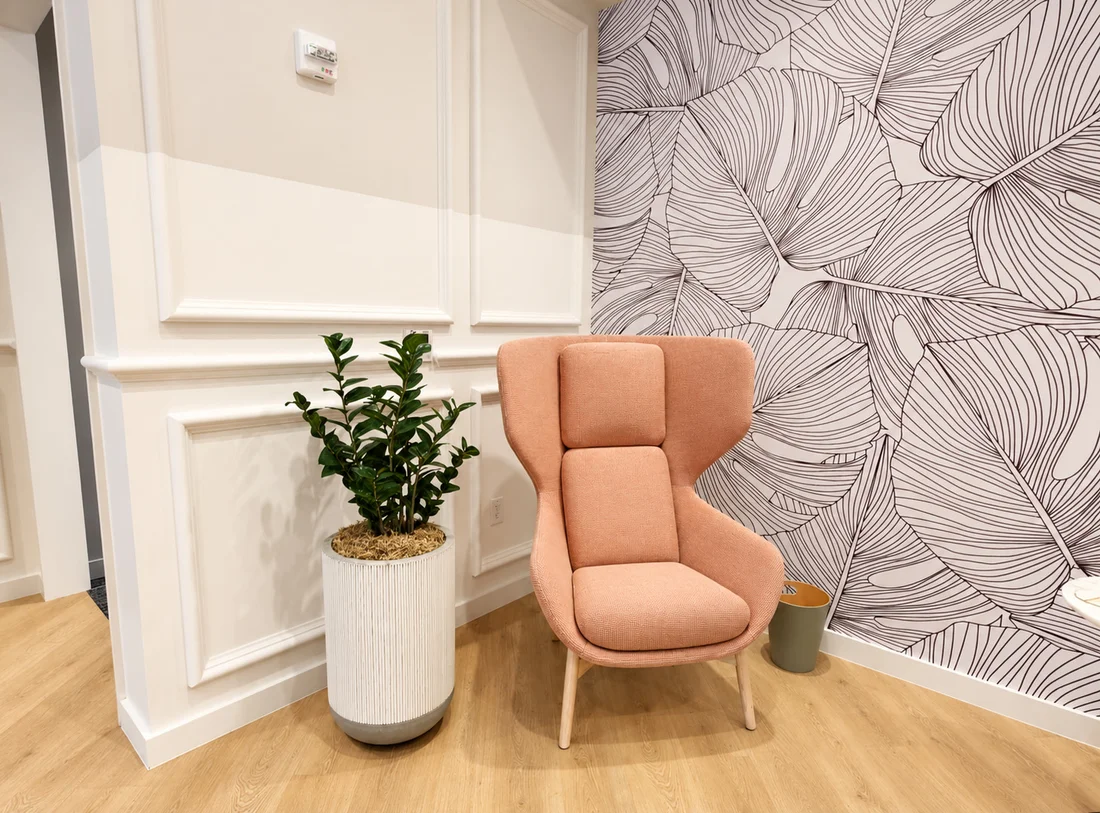 One Medical — Peach wing chair and a potted plant where white wall panelling meets the leaf-drawn wallpaper
