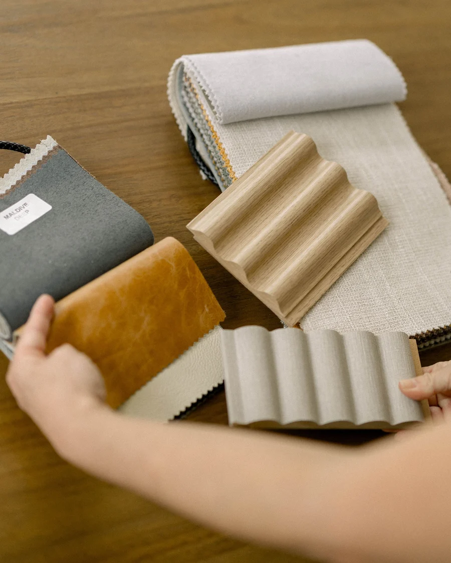 Hands arranging fabric, leather and fluted wood samples on a table
