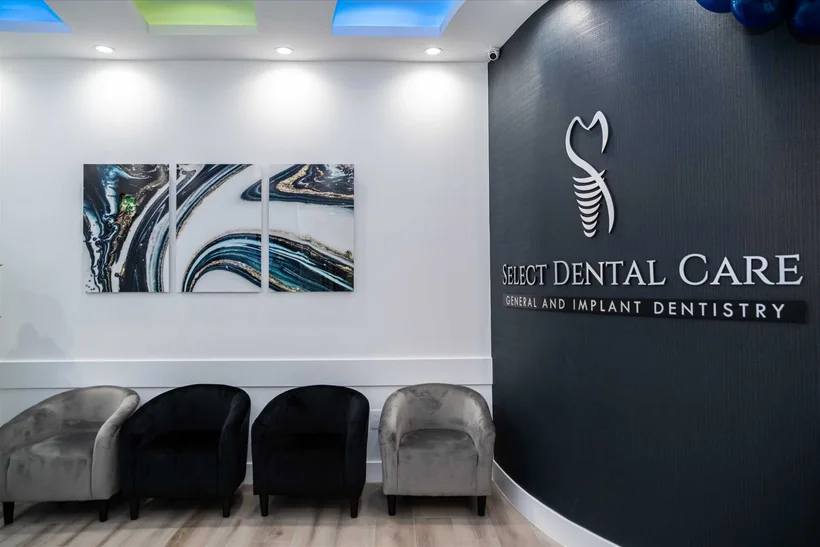 Select Dental Care — Recepción con el nombre de la clínica sobre una pared oscura, un tríptico de ágata y sillas de terciopelo gris y negro