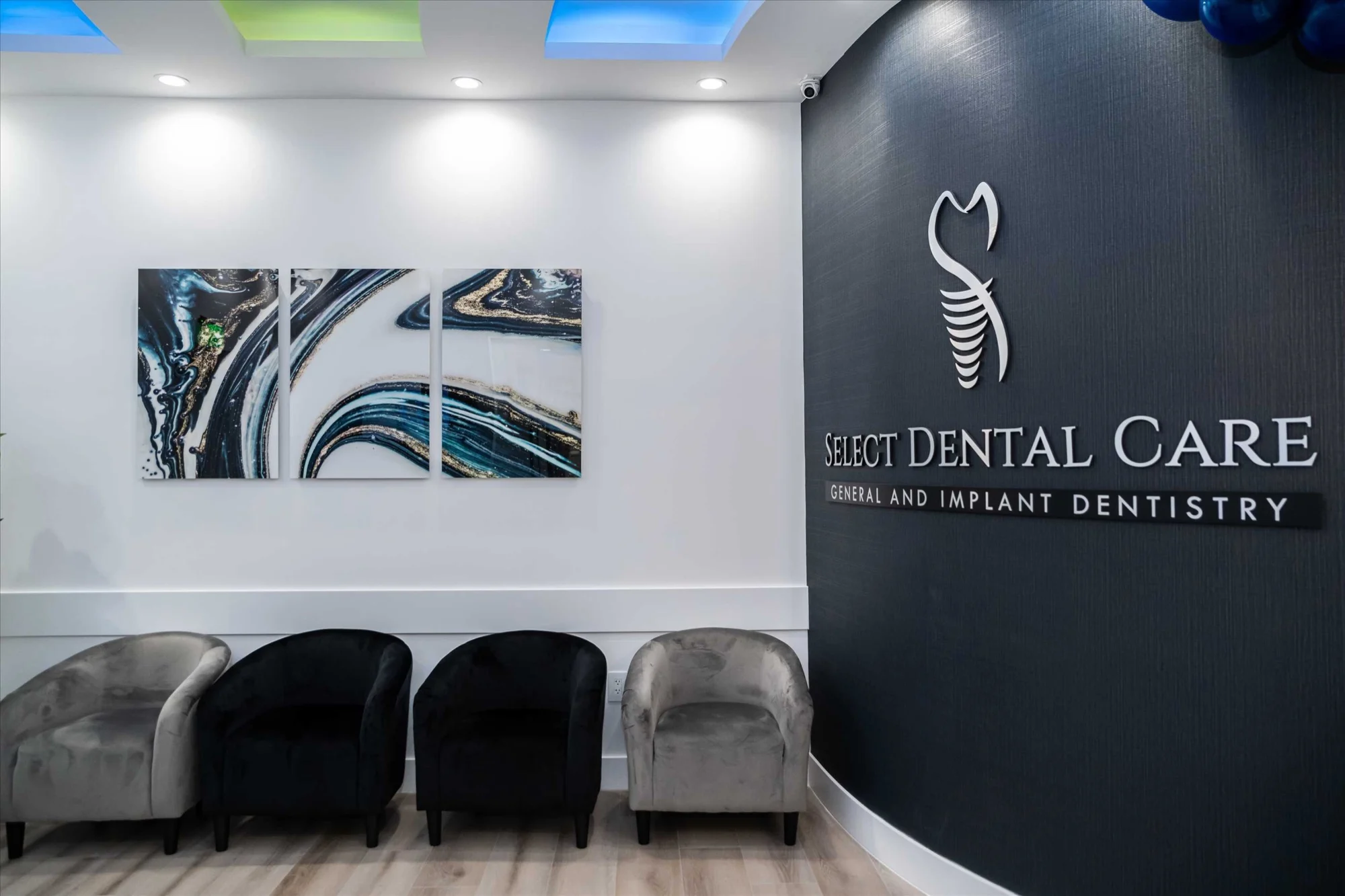 Select Dental Care — Recepción con el nombre de la clínica sobre una pared oscura, un tríptico de ágata y sillas de terciopelo gris y negro