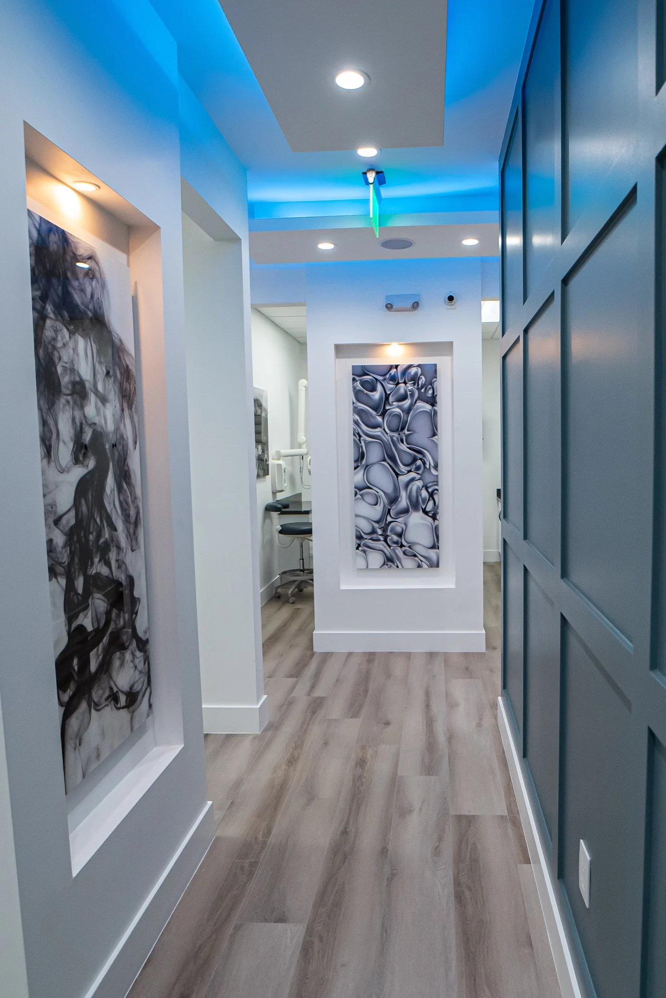 Select Dental Care — Pasillo con un muro oscuro de paneles a un lado y nichos de arte iluminados al fondo