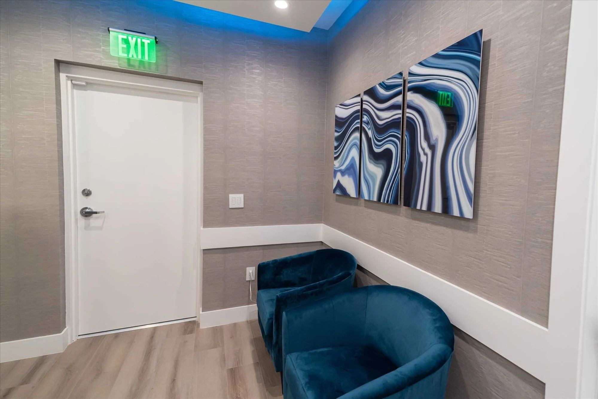 Select Dental Care — Rincón de espera con butacas de terciopelo azul bajo un tríptico de ágata azul y blanco