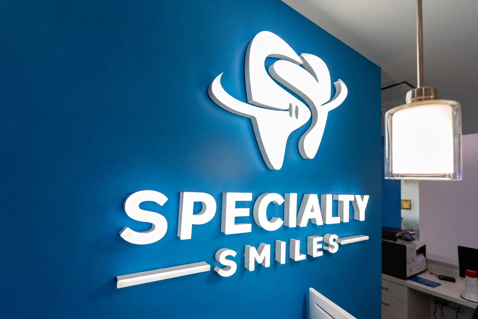 Specialty Smiles Orthodontics — Close-up of the white illuminated tooth logo and “Specialty Smiles” lettering on a blue wall