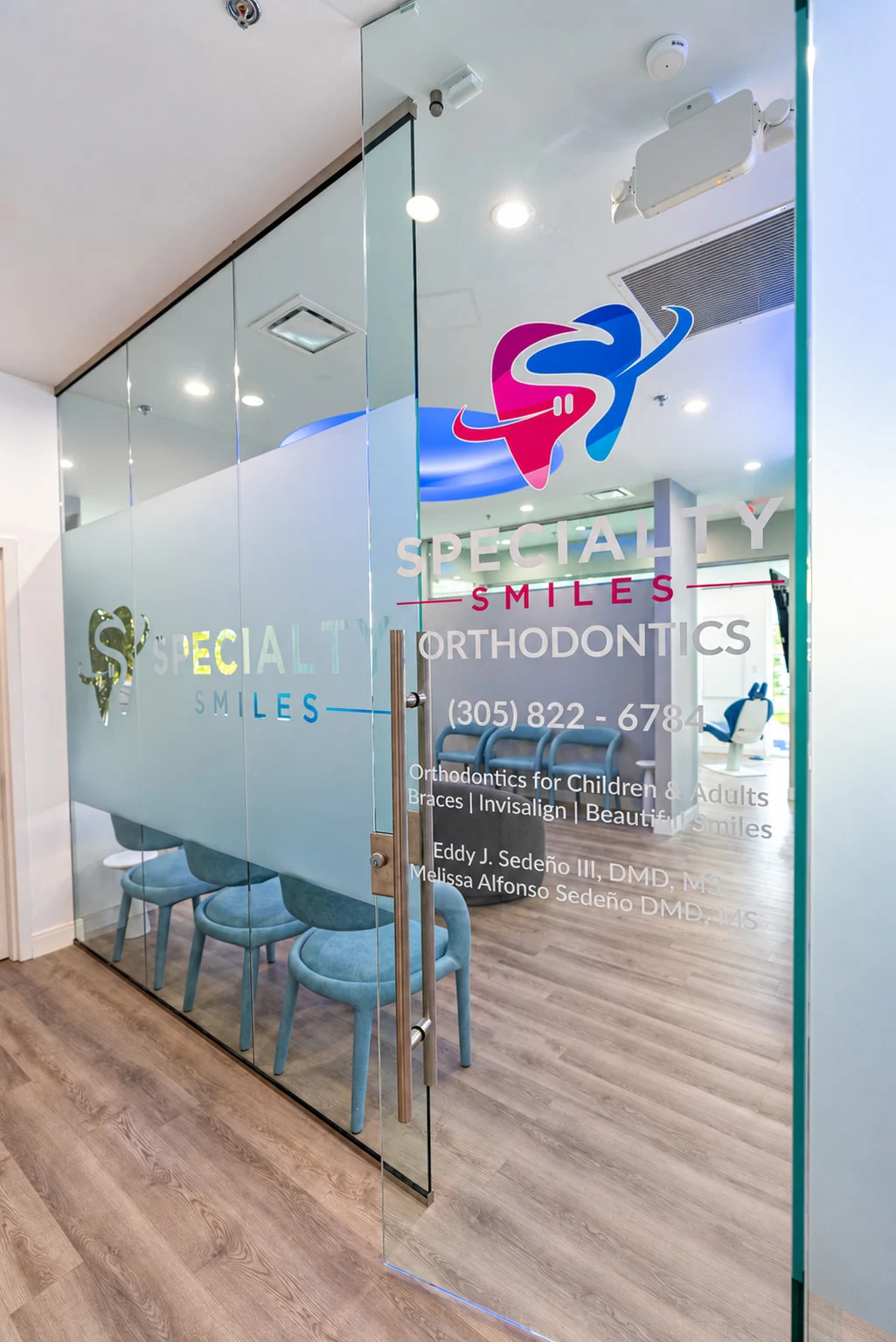 Specialty Smiles Orthodontics — Glass entrance with the color logo and “Orthodontics for Children & Adults” in vinyl, light blue chairs behind